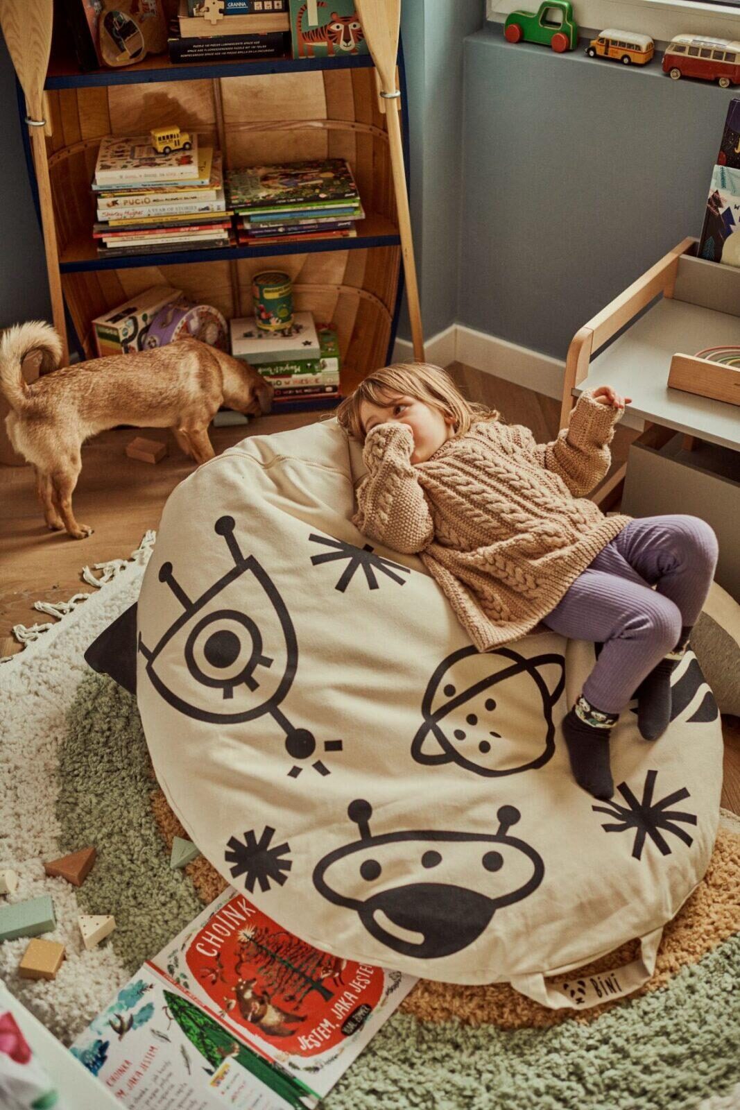 Pufe Bini Grande FOGUETÃO Saco de feijão bege com desenhos espaciais a preto numa sala infantil e criança deitada em cima