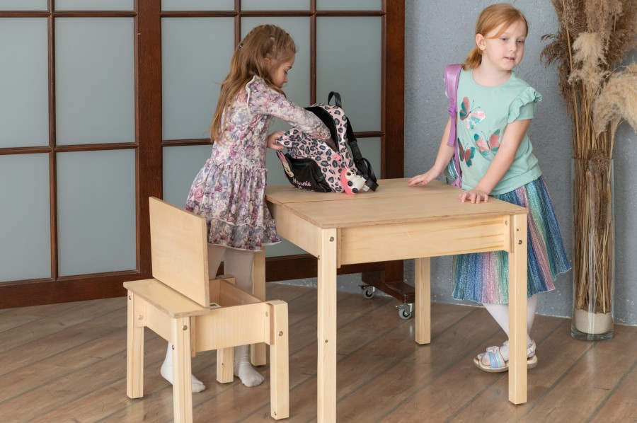 Conjunto de Mesa e Cadeira Infantil com Arrumação Mesa e cadeira infantis de madeira natural clara com duas meninas envolvidas