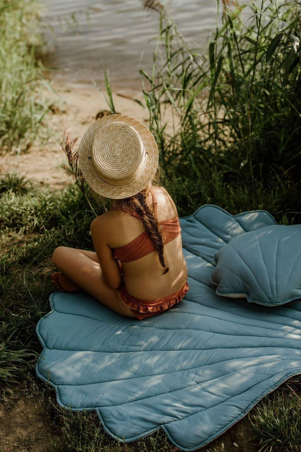 Tapete de Linho CONCHA Colchão azul em forma de concha com menina sentada de chapéu de palha junto a lago