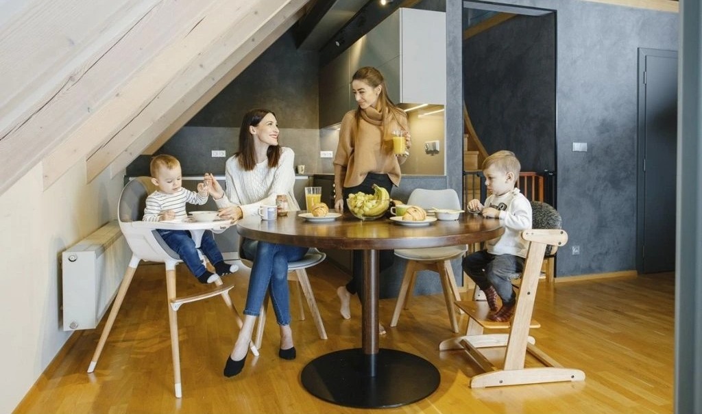 Mesa de jantar redonda em madeira escura com cadeiras de madeira clara e cadeiras altas para crianças