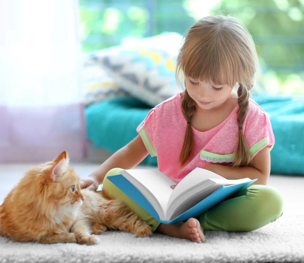 Os Benefícios de as Crianças Lerem para os Seus Animais de Estimação Menina a ler livro sentada no chão com gato ruivo ao lado