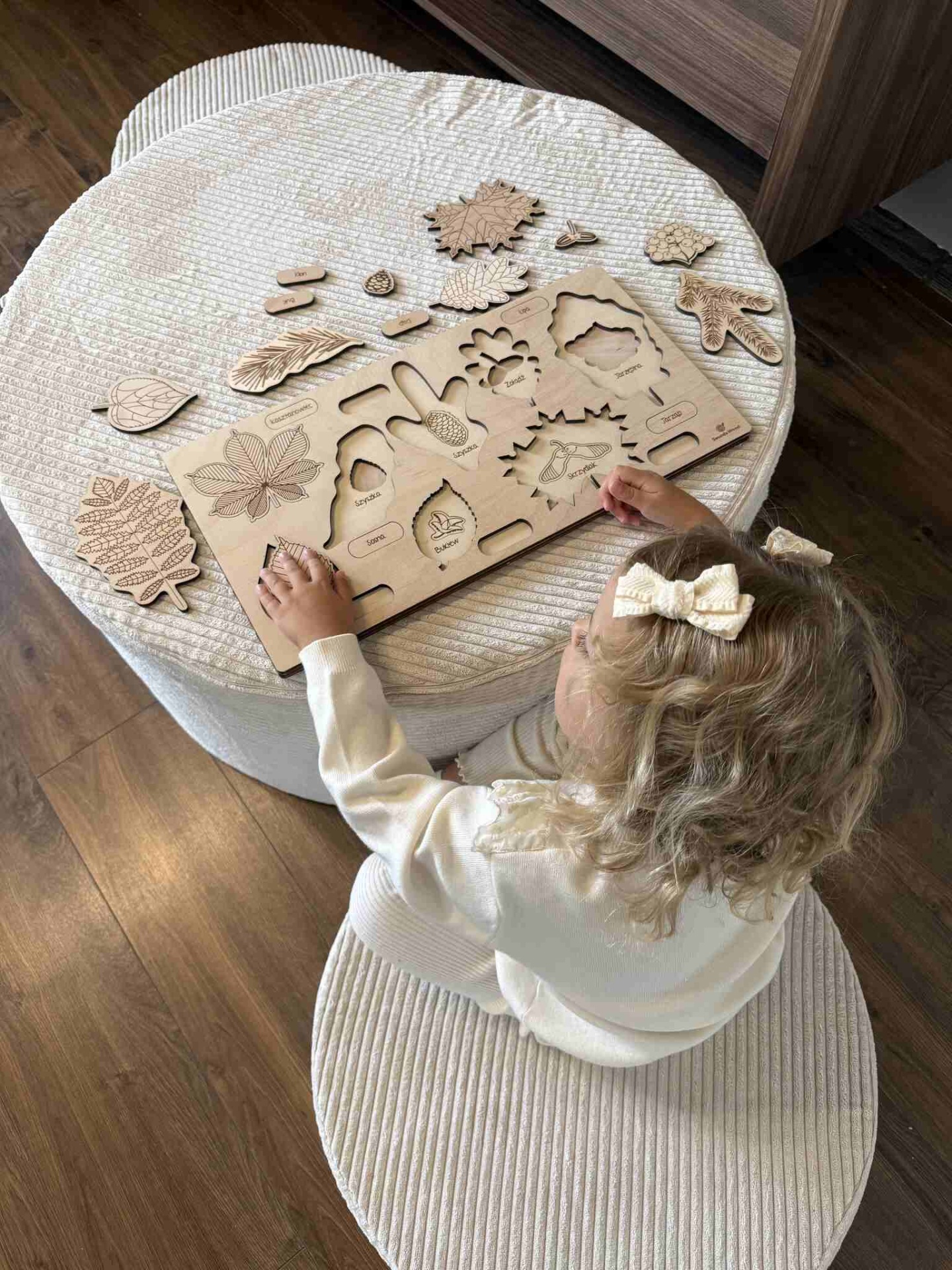 Conjunto Pufe Modular em Veludo Cotelê Bege Criança brincando com quebra-cabeças de madeira com formas de folhas e pinhas