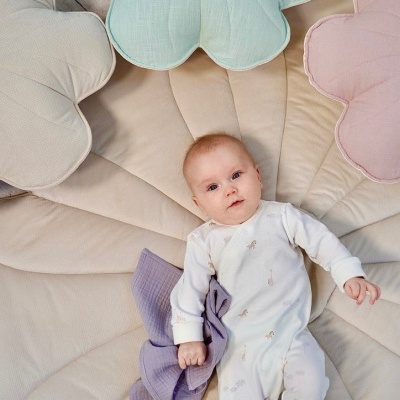 Bebé deitado em almofada grande em forma de folha com almofadas florais ao redor