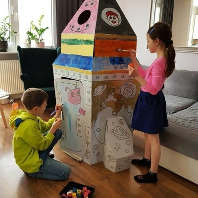 Crianças a pintar foguete de papelão colorido com astronautas e planetas numa sala
