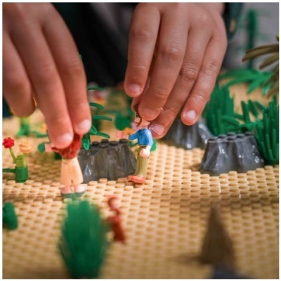Duas figuras de brinquedo em plástico num cenário amarelado com plantas e rochas artificiais.