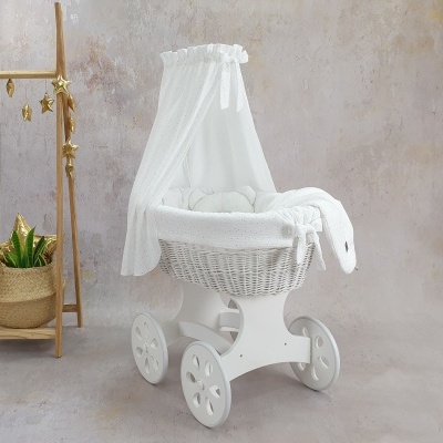 Berço de bebé branco com dossel e almofadas, junto a planta e cabide decorativo