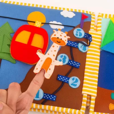 Livro sensorial em tecido com girafa marioneta dedo e cenário colorido com números e teleférico.
