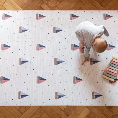 Tapete infantil com padrão de triângulos coloridos, criança a brincar e xilofone sobre chão de madeira