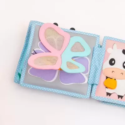 Livro infantil tecido com borboleta colorida e vaca desenhada