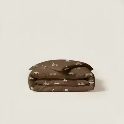 Colcha infantil castanha com carrinhos e motas dobrada sobre superfície clara