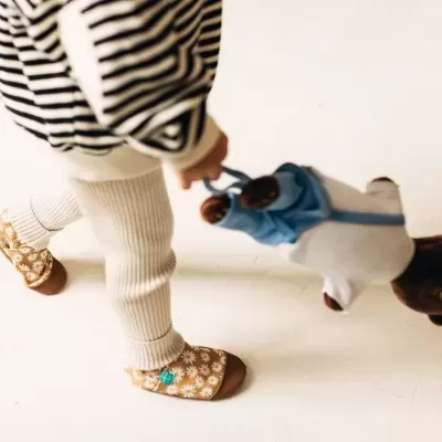 Criança com roupas às riscas e sapatos com padrão de margaridas a segurar ursinho de peluche