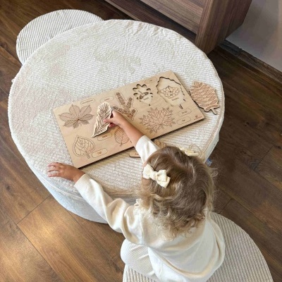 Quebra-cabeças educativo de madeira com folhas e frutas, criança brinca em mesa branca texturizada.