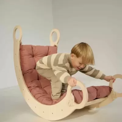 Baloiço de madeira clara com almofada rosada e menino loiro a brincar.