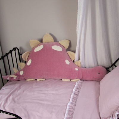 Travesseiro em forma de dinossauro rosa numa cama com roupa de cama rosa