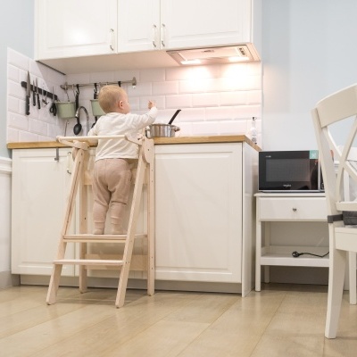 Criança em cozinha branca usando banco de madeira para alcançar bancada