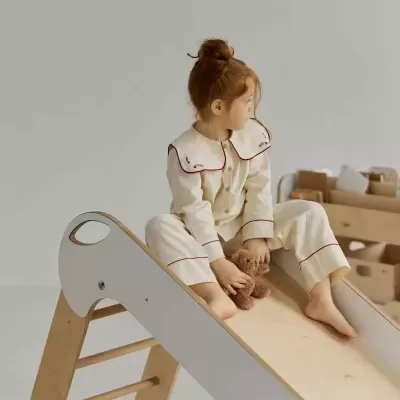 Menina sentada numa rampa de madeira vestida com pijama creme