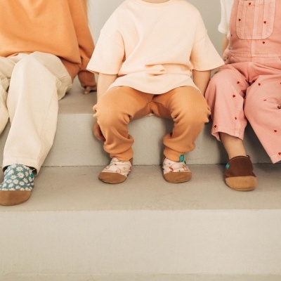 Crianças sentadas com calças coloridas e sapatinhos de tecido