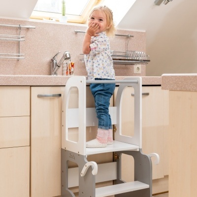 Criança em banquinho de aprendizagem na cozinha com degraus e rodas.