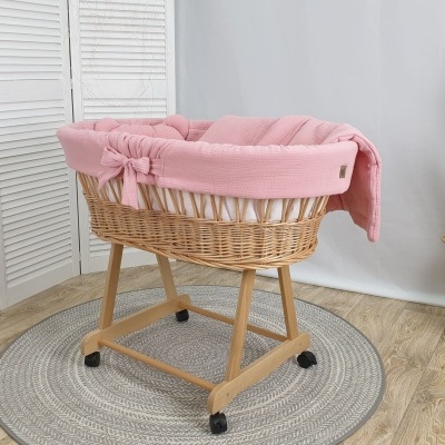 Berço moisés em vime com tecido rosa claro em ambiente com planta e piso de madeira