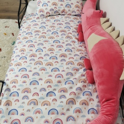 Cama com roupa de cama com padrão de arco-íris e almofada decorativa rosa em forma de dinossauro