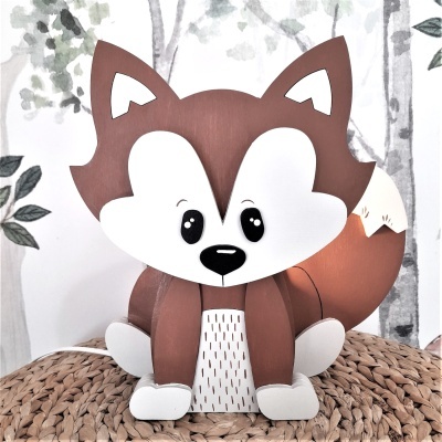 Figurinha decorativa de raposa castanha e branca, olhos grandes pretos, sobre tecido trançado natural, fundo com árvores em preto e branco