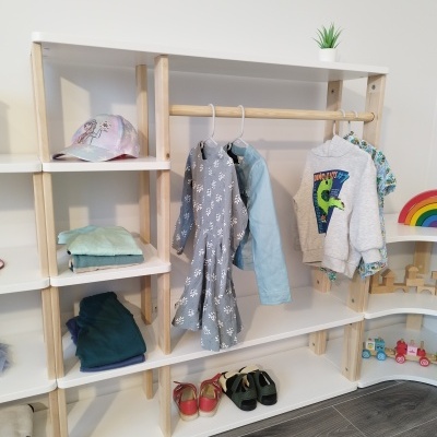 Estante branca e madeira clara com roupas infantis e brinquedos