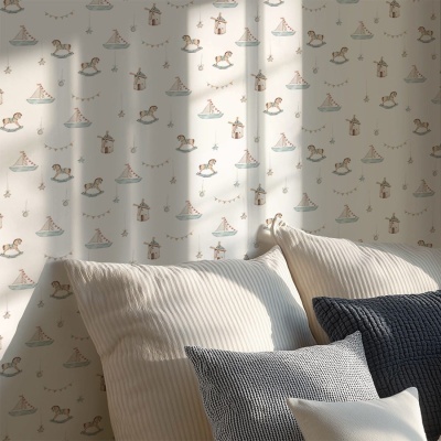 Parede com papel de parede infantil com cavalos de baloiço, barcos e moinhos, cama com almofadas creme e azul escuro.