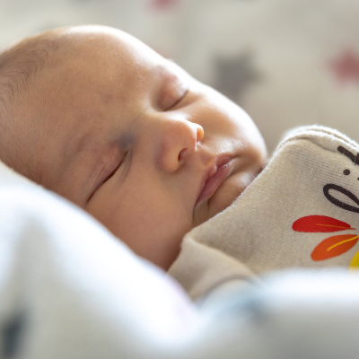 Recém-nascido a dormir com roupa bege e padrão de folhas