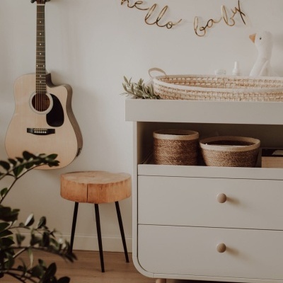 Canto de quarto com guitarra, banco de madeira, cómoda branca e decoração 'hello baby'