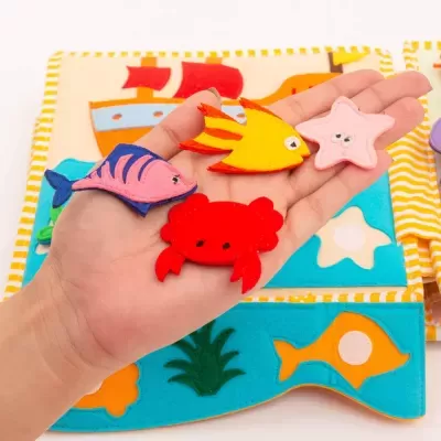 Figuras de animais marinhos em feltro em mão sobre fundo de tecido azul com motivos marinhos.