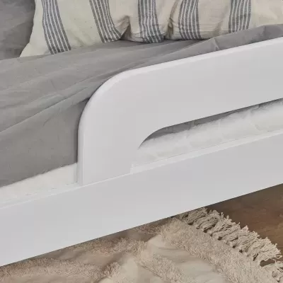 Cama branca com colchão e roupa de cama cinza, almofadas listradas e tapete bege com franjas