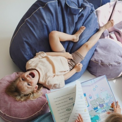 Criança deitada em almofada rosa com almofadas ao redor e livro aberto
