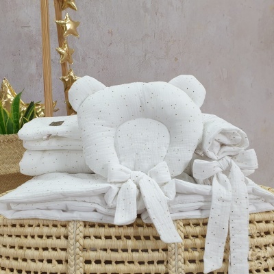 Conjunto de roupa de bebé branco com padrão dourado em almofada em forma de ursinho sobre cesto trançado