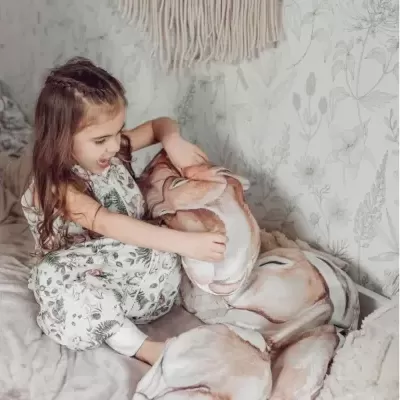 Menina com pijama floral segurando almofada grande com estampa de cervo na cama
