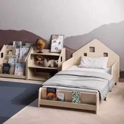 Quarto infantil com cama em madeira clara, roupas de cama cinza, estante com livros e brinquedos, parede com pintura abstrata