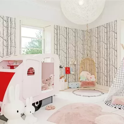 Quarto infantil com cama forma caravana, parede com padrão troncos de árvore, cadeira suspensa, tenda branca e tapetes rosa.