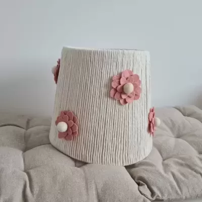 Abajur branco texturizado com flores cor-de-rosa e botões brancos numa superfície almofadada cinza