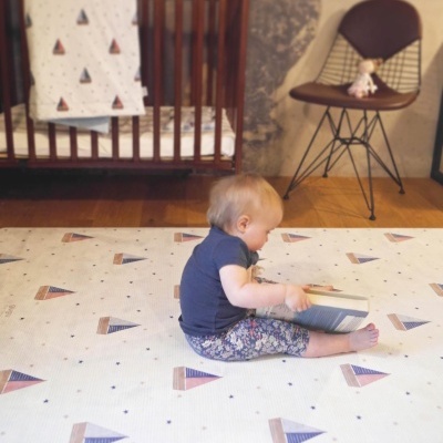 Tapete para bebé com padrão de triângulos coloridos em sala com berço e cadeira
