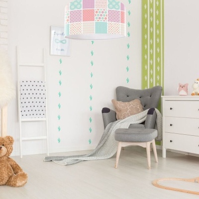 Quarto infantil com poltrona cinzenta, candeeiro colorido e cómoda branca