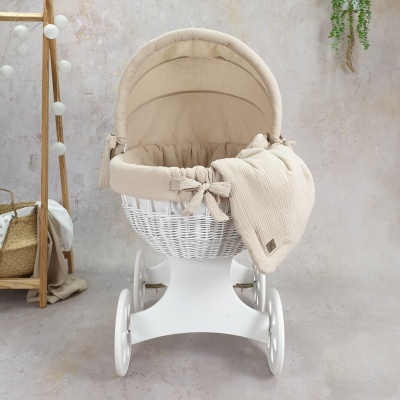 Carrinho de bebé de vime branco com forro bege e manta bege num ambiente interior moderno.