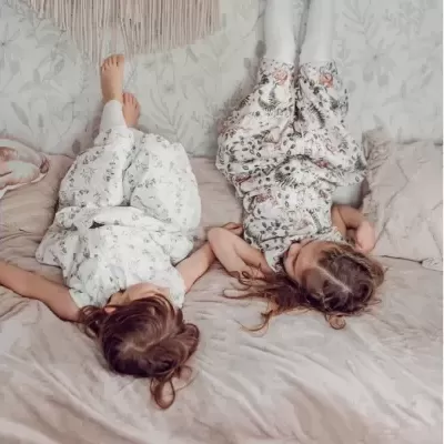 Crianças de pijamas florais deitadas de cabeça para baixo numa cama com almofadas