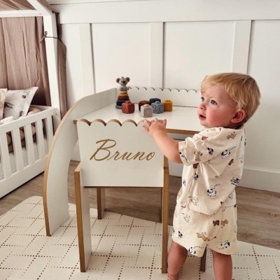 Móveis infantis personalizados com nome Bruno, criança usando pijama bege com padrões, brinquedos em mesa branca, tapete bege quadriculado