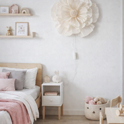 Quarto infantil com decoração clara, camas com almofadas cor-de-rosa e cinza e candeeiro de parede em forma de flor branca.