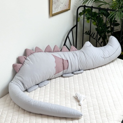 Almofada crocodilo cinzento e rosa numa cama com colchão bege e estrutura preta