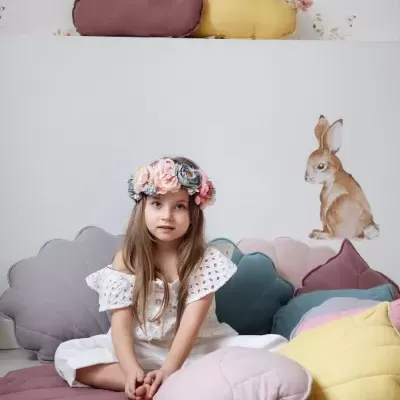 Almofadas coloridas em forma de nuvem e flor numa sala infantil com papel de parede floral e adesivo de coelho