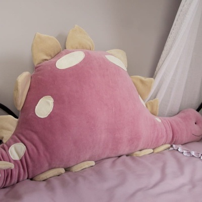 Almofada em forma de dinossauro cor-de-rosa sobre cama cor-de-rosa