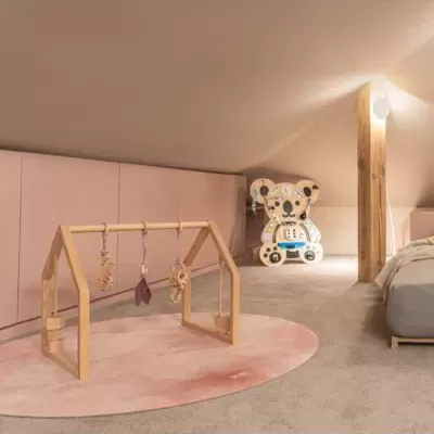 Quarto infantil com tapete rosa, brinquedo de madeira pendurado e urso de brinquedo ao fundo