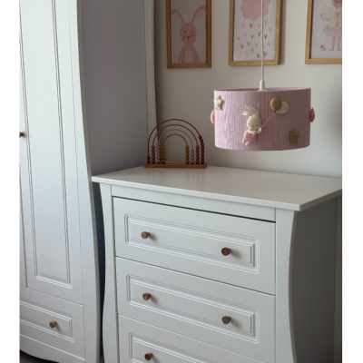 Cômoda branca de madeira com três gavetas e luminária rosa decorada com coelho