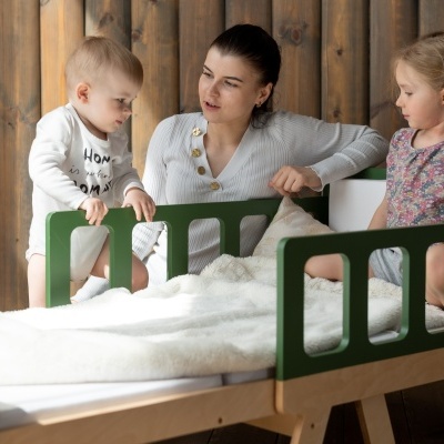 Berço infantil verde e madeira clara com roupa branca e família ao redor