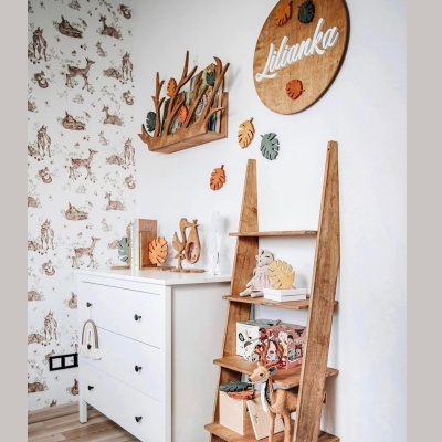Quarto infantil com cómoda branca, estante de madeira, brinquedos e placa redonda de madeira com texto Lilanka